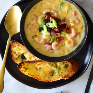 A bowl of bacon shrimp and corn chowder with two slices of toast.
