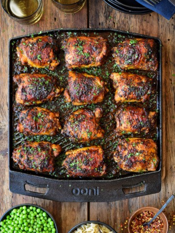 A top down image of twelve crispy chicken thighs on an Ooni Grizzler pan.