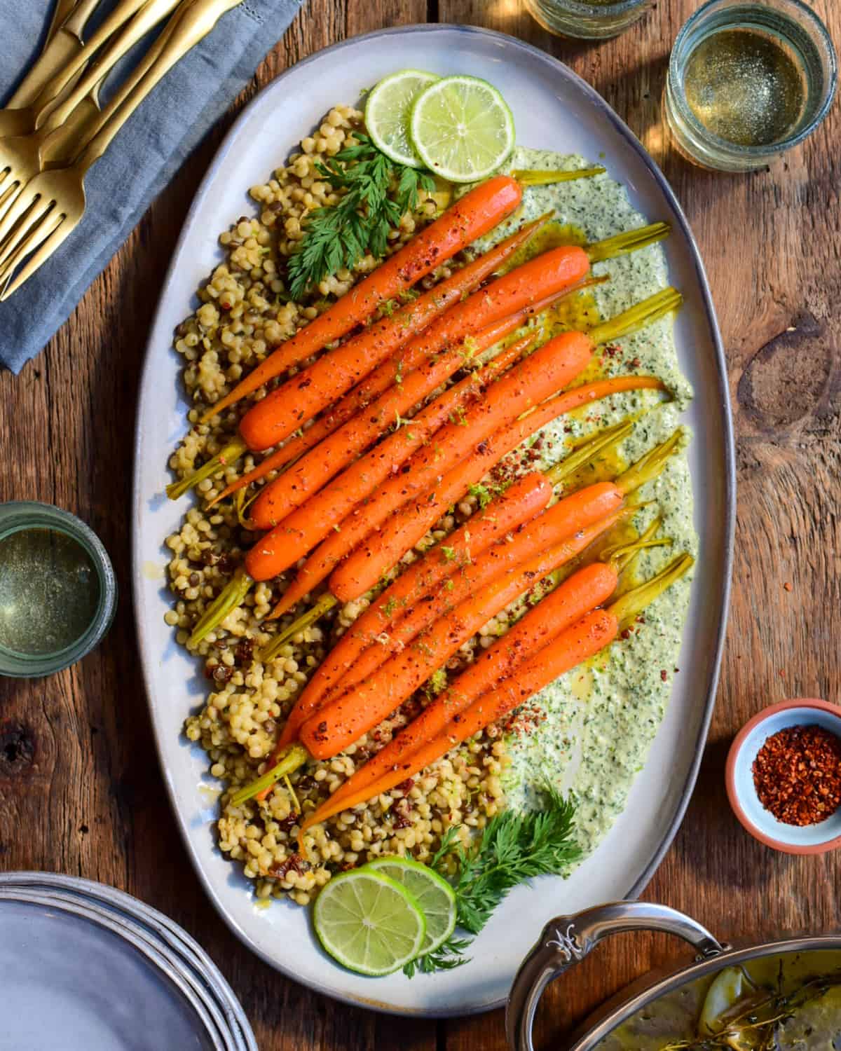 A platter of fancy carrots served over a carrot top tahini sauce and couscous.