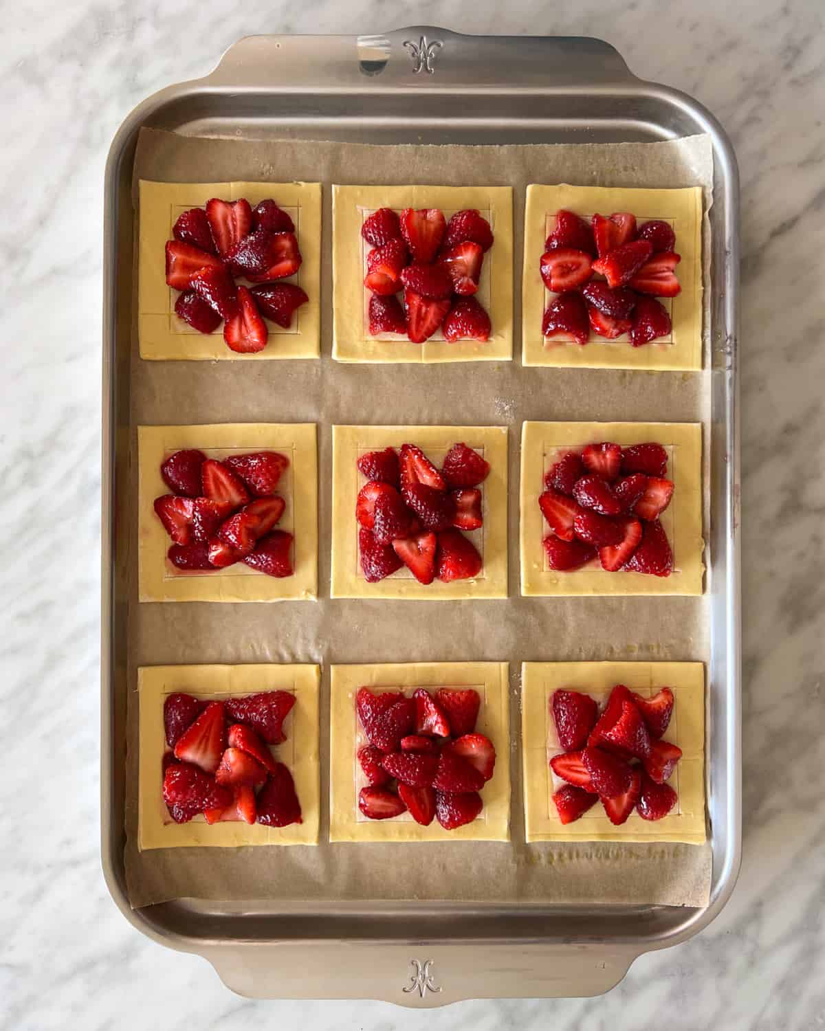 Nine puff pastry square with strawberries placed in the center ready to go into the oven.