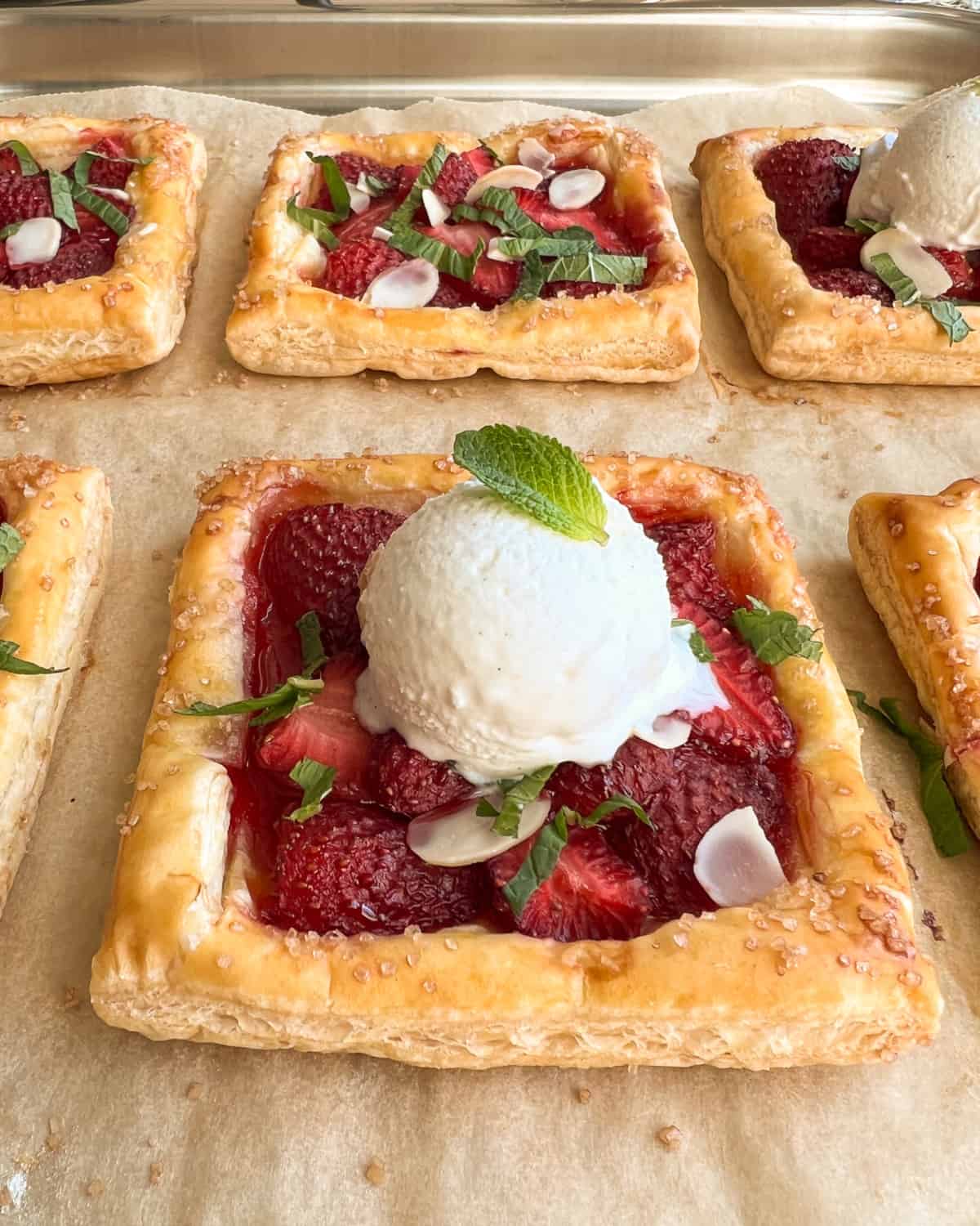 A close up of a fresh strawberry tart served with a scoop of ice cream and mint.