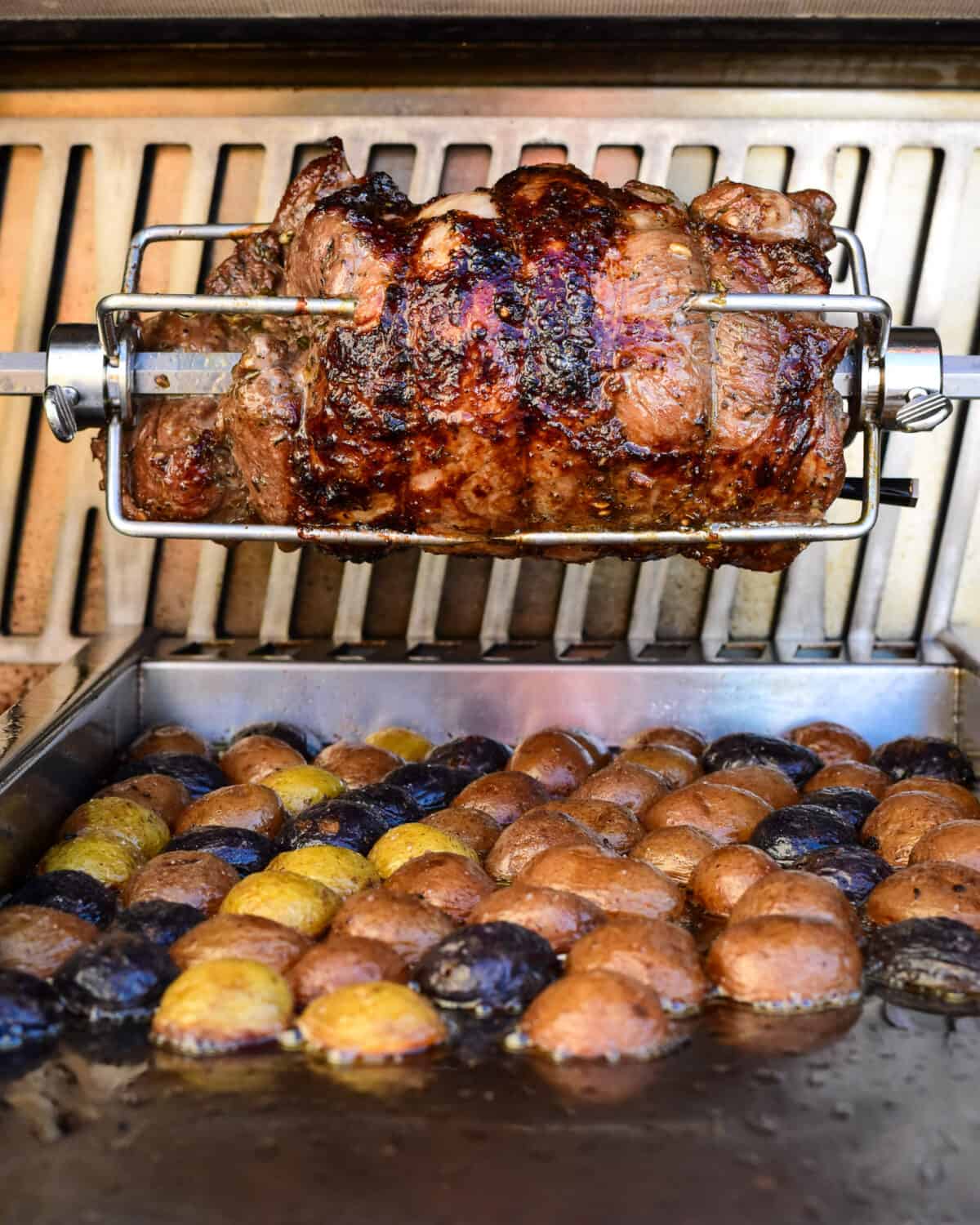 A Easter boneless leg of lamb on the rotisserie with potatoes cooking in the drippings.