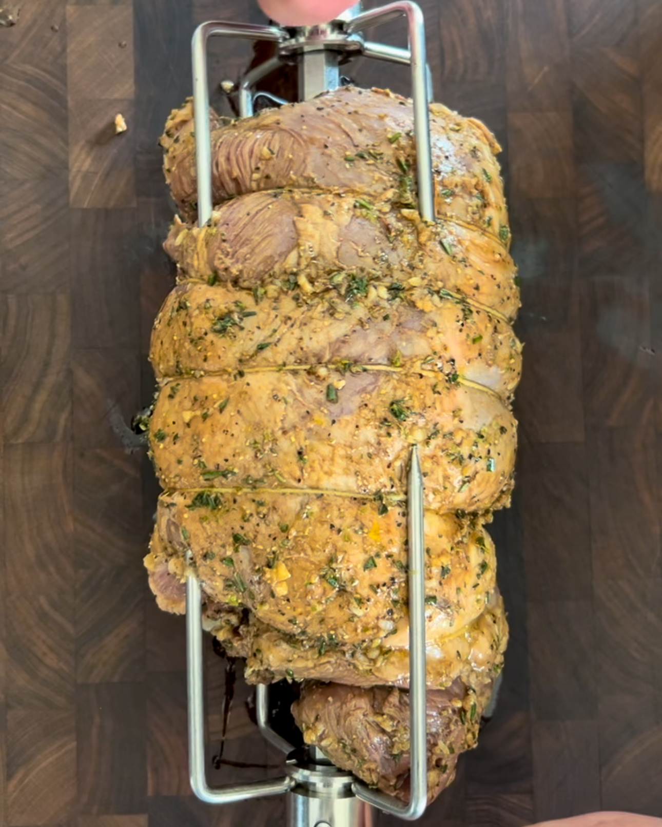 Slide the spit of the rotisserie through the center of the lamb and secure both ends with rotisserie forks.