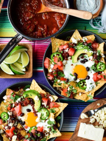 Two chilaquiles breakfast bowls with a sunny side up egg and other colourful toppings.