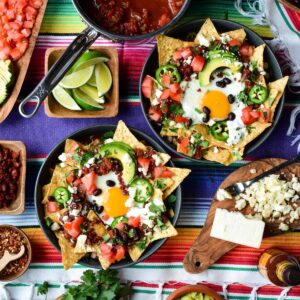 Two chilaquiles breakfast bowls with a sunny side up egg and other colourful toppings.