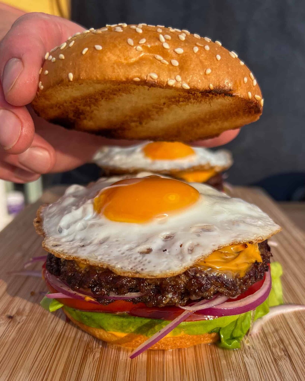 A double smash burger with a fried egg on top getting topped with a sesame seed bun.