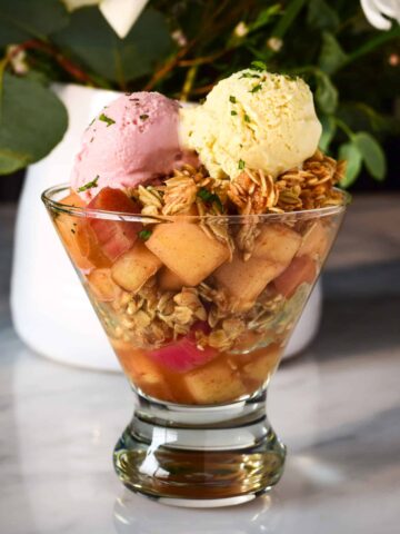 A glass filled with sous-vide apples, rhubarb and granola with two scoops of ice cream.