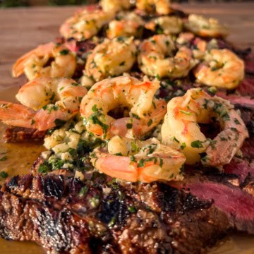 A grilled flank steak topped with garlic shrimp.