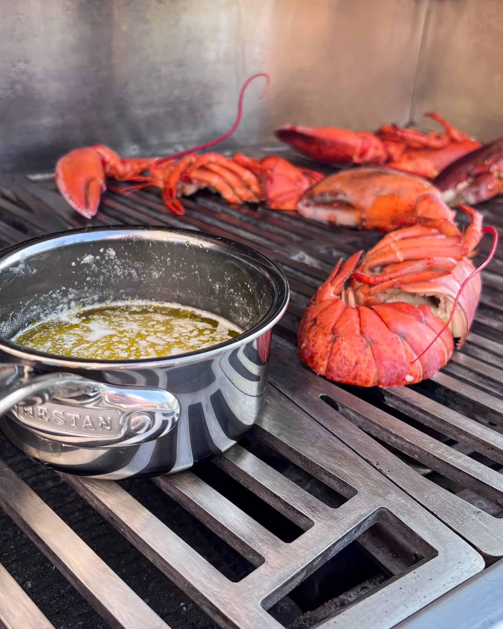Lobster halves grilling with a pot of butter. 