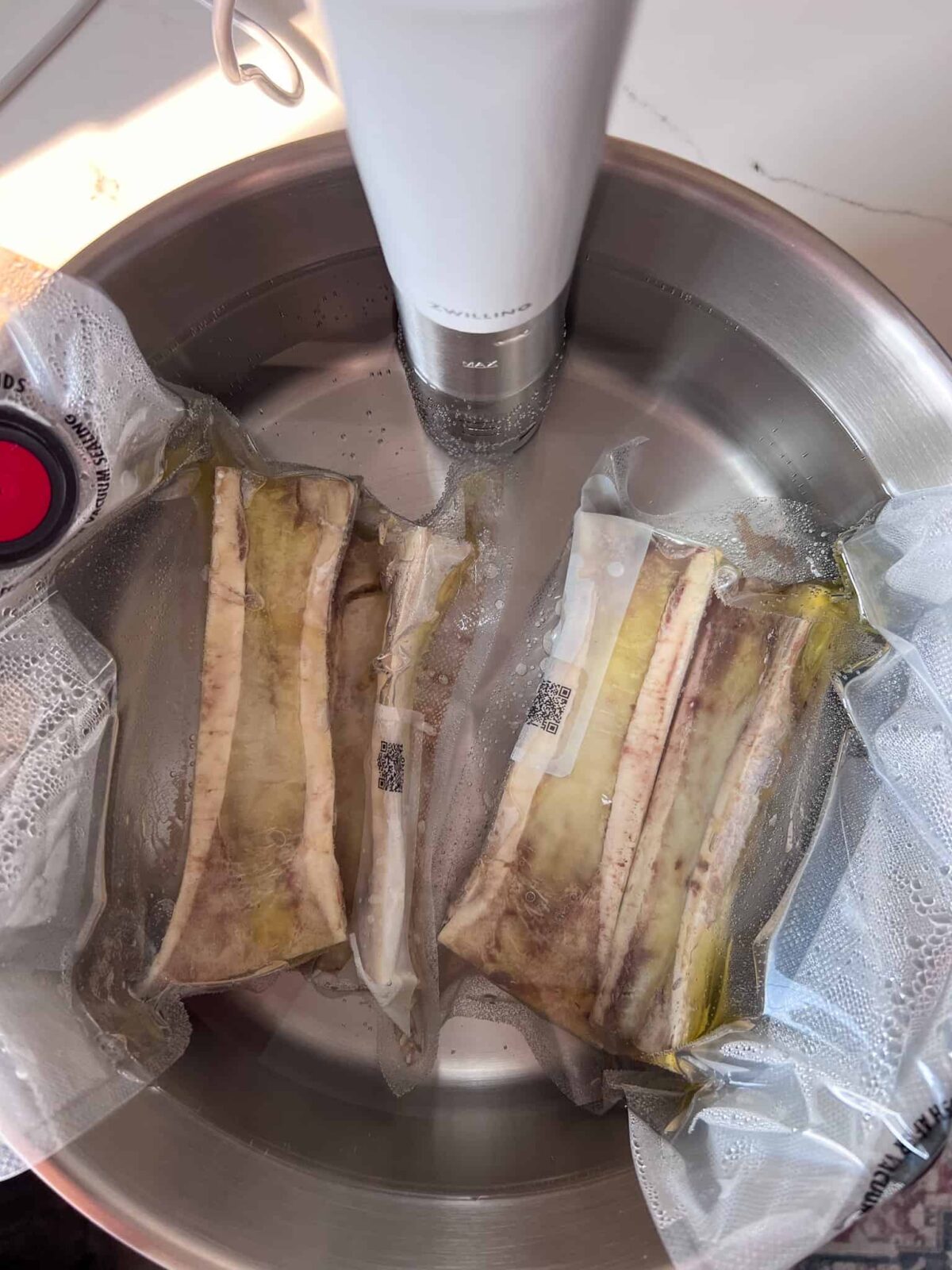 Two bags of bone marrow submerged in a sous vide water bath.