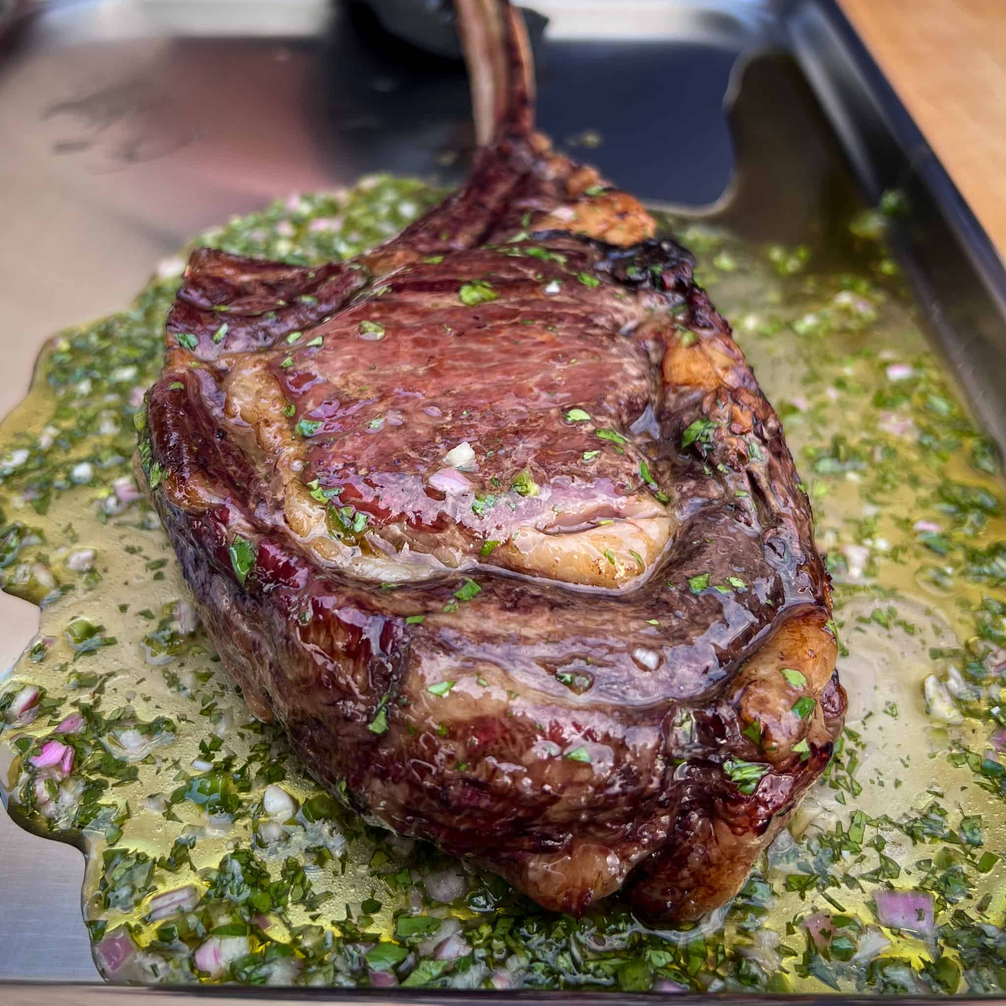A grilled bison frenched ribeye steak on a tray with a fresh herb sauce.