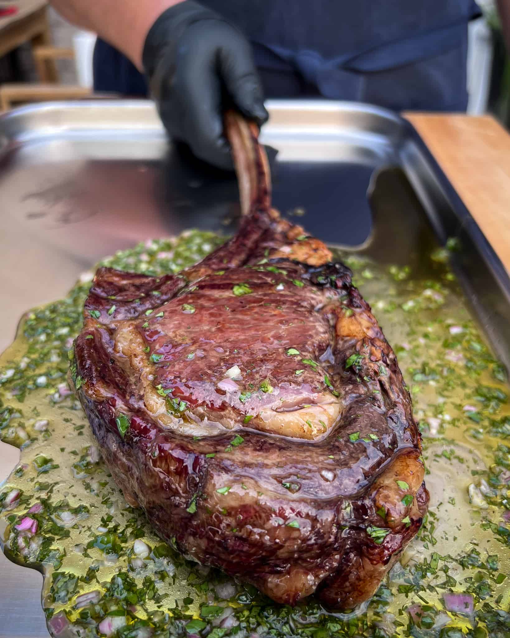 A grilled bison frenched ribeye steak on a tray with a fresh herb sauce.