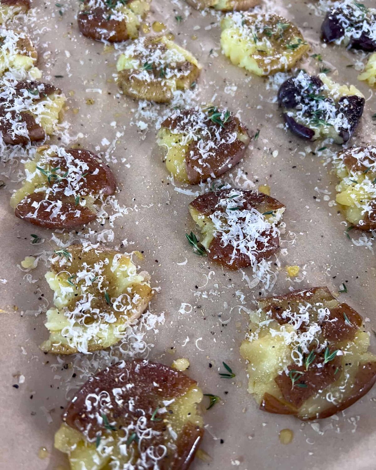 A tray of smashed potatoes sprinkled with parmesan cheese, fresh thyme, salt, pepper and garlic powder. 