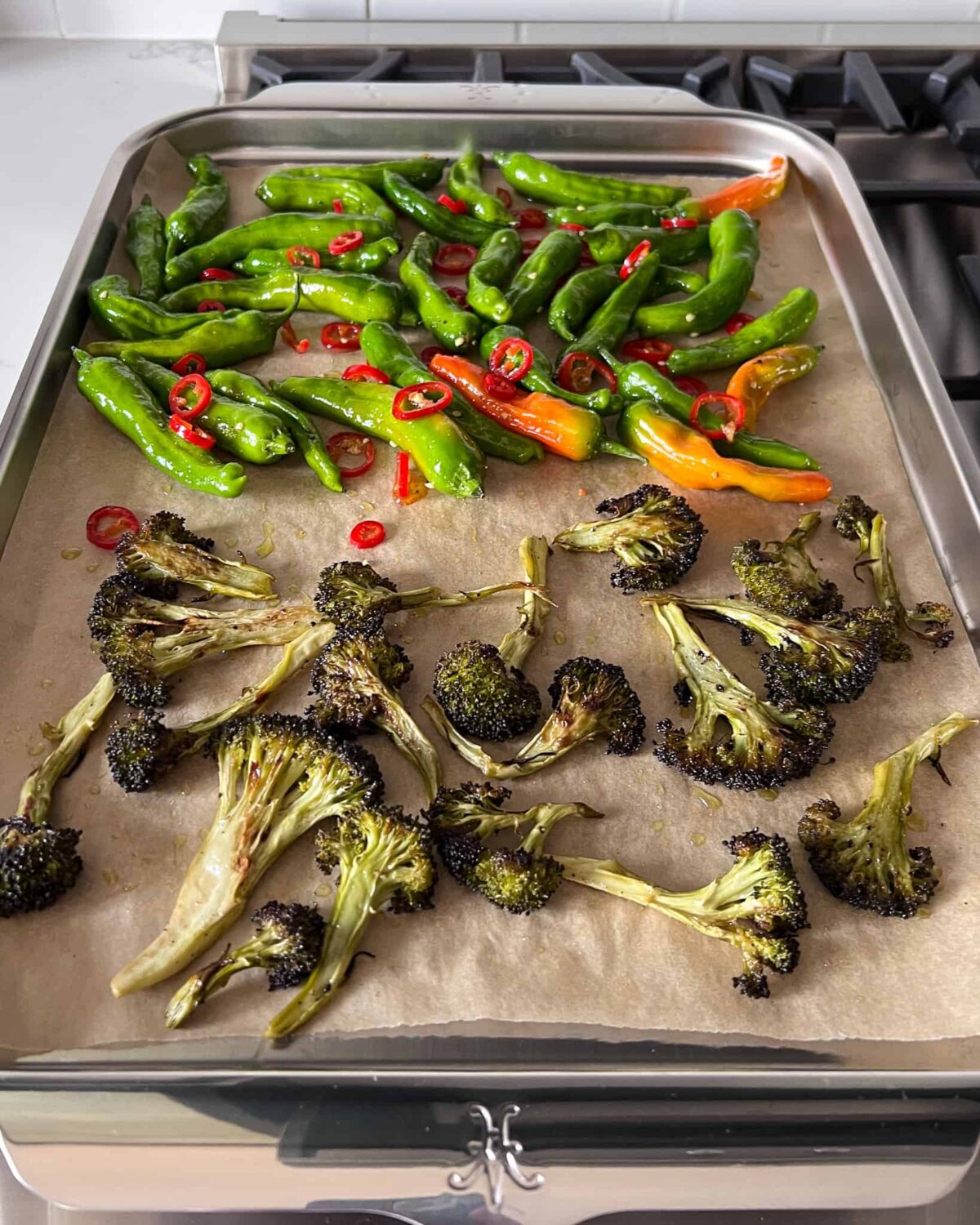 A sheet pan with shishitos and long red chilies slices on the one half, with roasted broccolini on the other half.