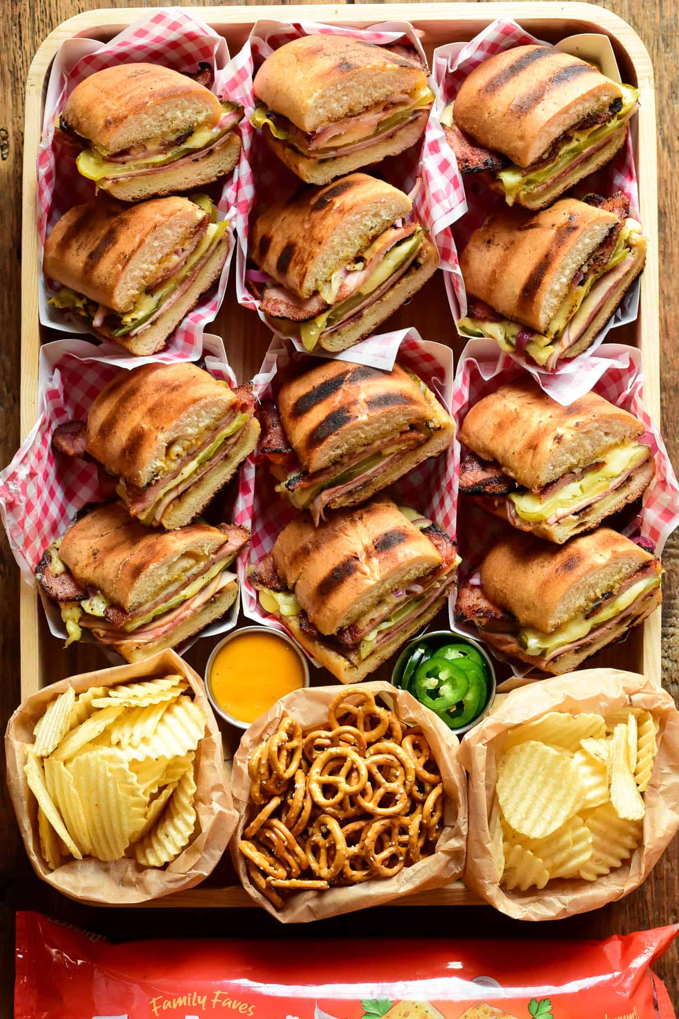 A tray of grilled Cuban sandwiches (Cubano) with chips and pretzels.