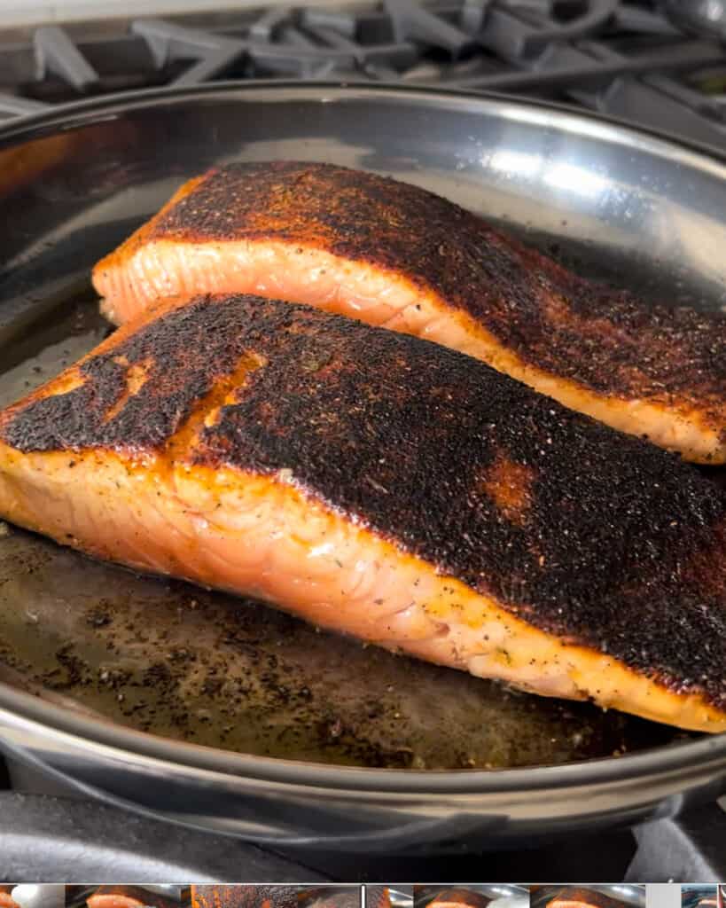 Two piece of seared blackened salmon in a pan.