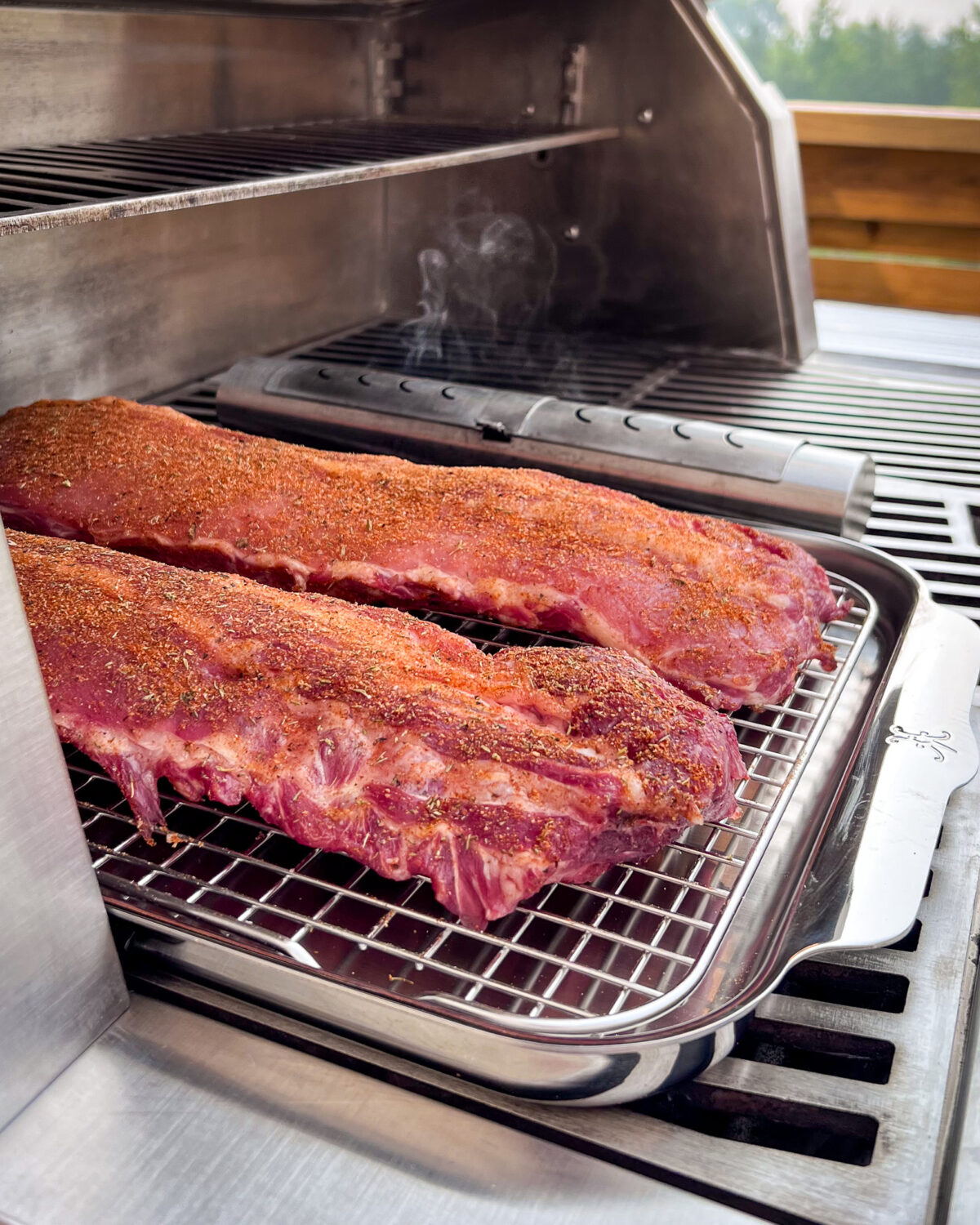 Two racks of ribs, meat side up, on a half sheet pan with a rack placed on the grill.
