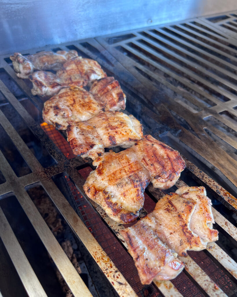 Six grilled chicken thighs on the BBQ.