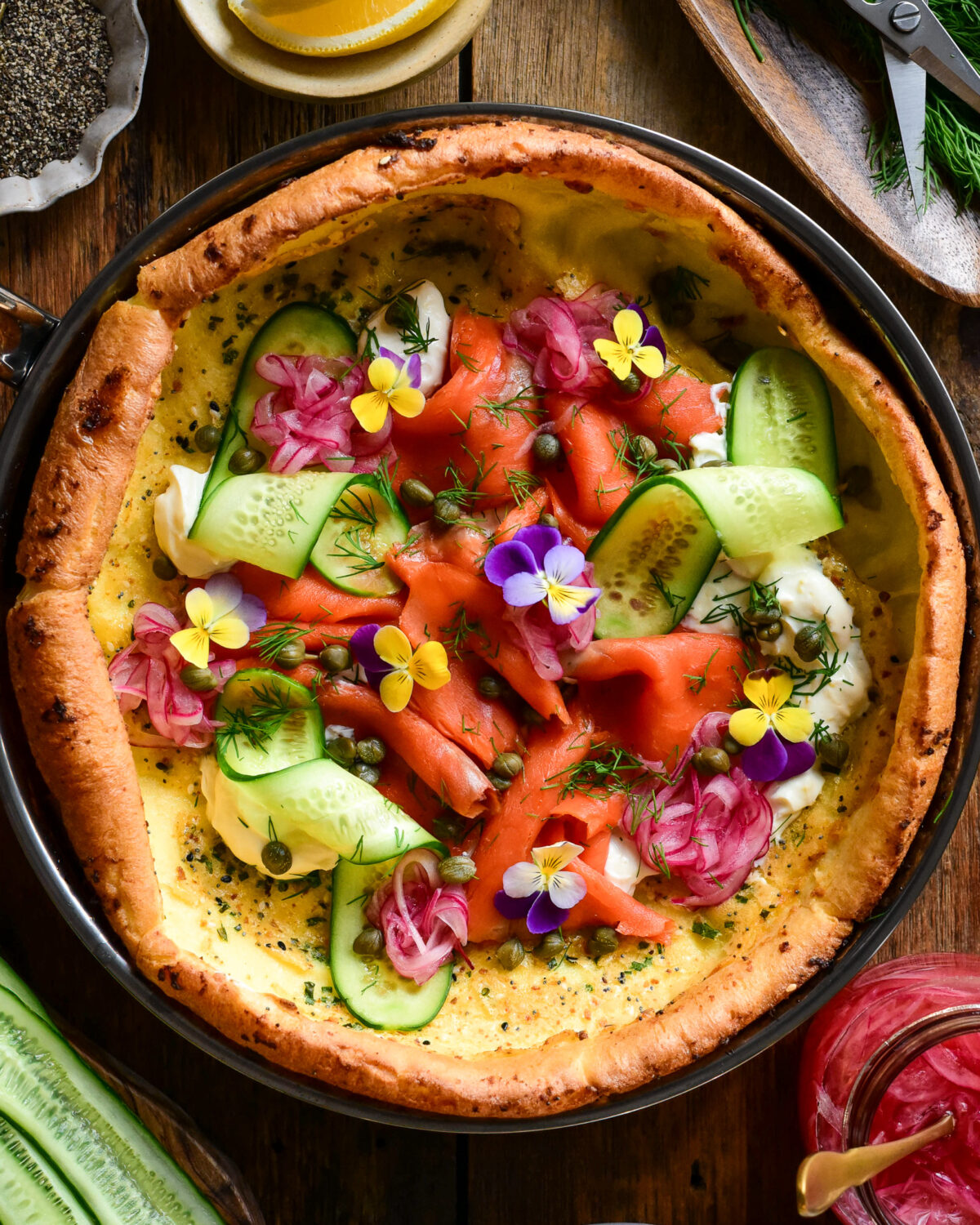 A Savory Dutch Baby with Smoked , , cream cheese, capers, pickled onions, cucumber, fresh herbs, everything bagel seasoning and edible flowers.