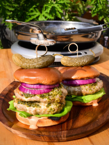 Two skillet burgers with chimichurri on a wooden plate. One is a double skillet cheeseburger.