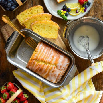 A Zucchini Lemon Loaf sliced with glaze. Served with fresh fruit and edible flowers.