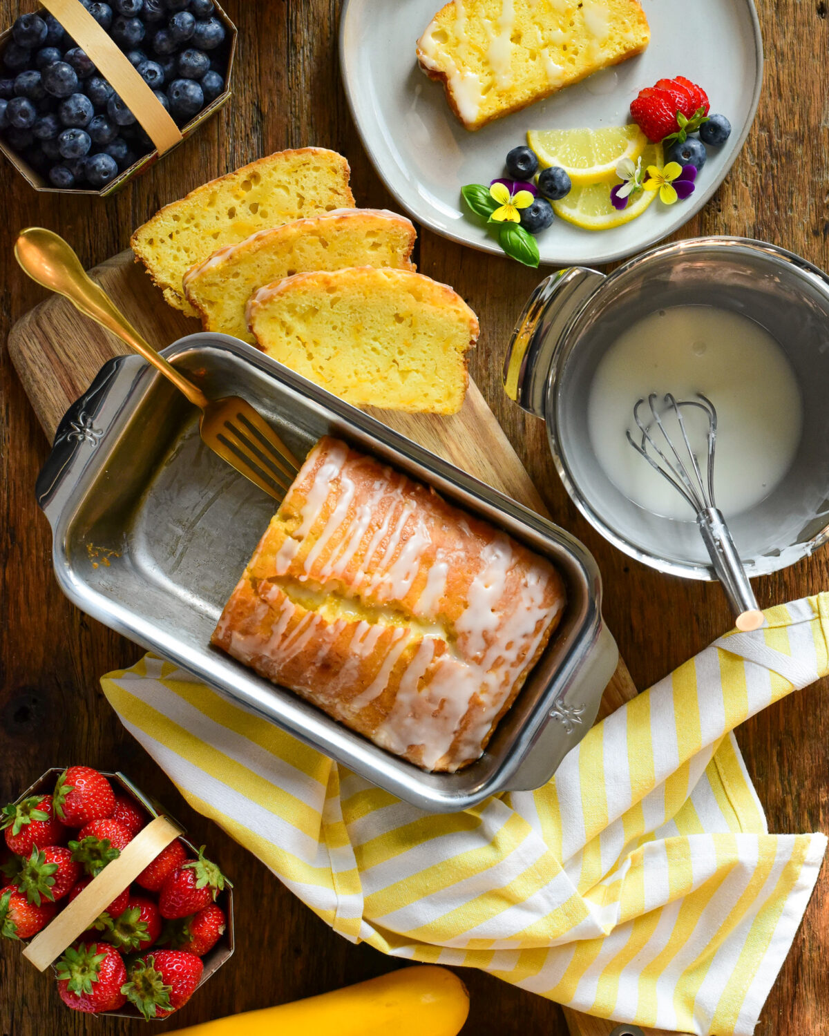 A Zucchini Lemon Loaf sliced with glaze. Served with fresh fruit and edible flowers.