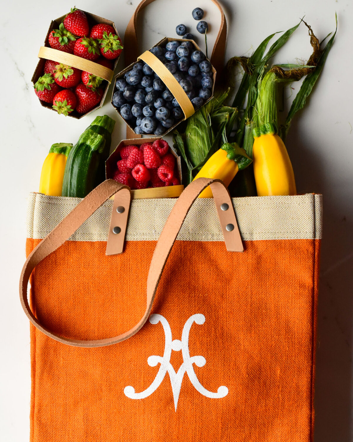 An orange market bag with fresh berries and vegetables.
