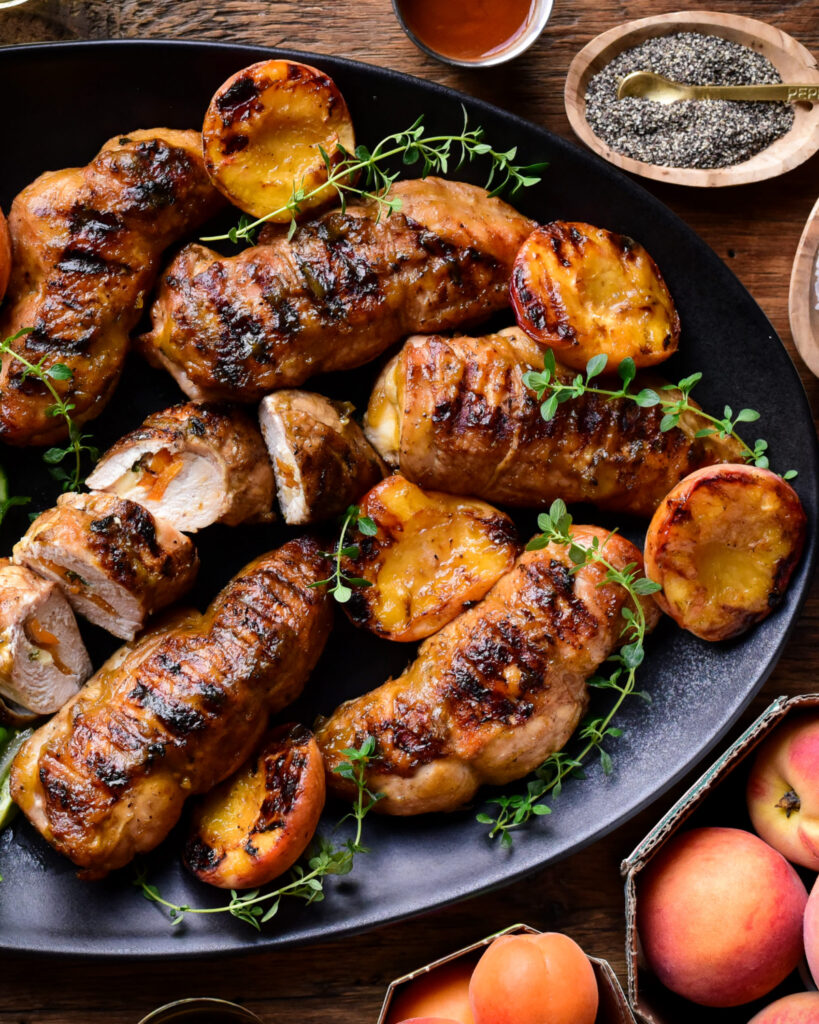 A platter of grilled chicken and peaches. The chicken is stuff with apricots and Brie.
