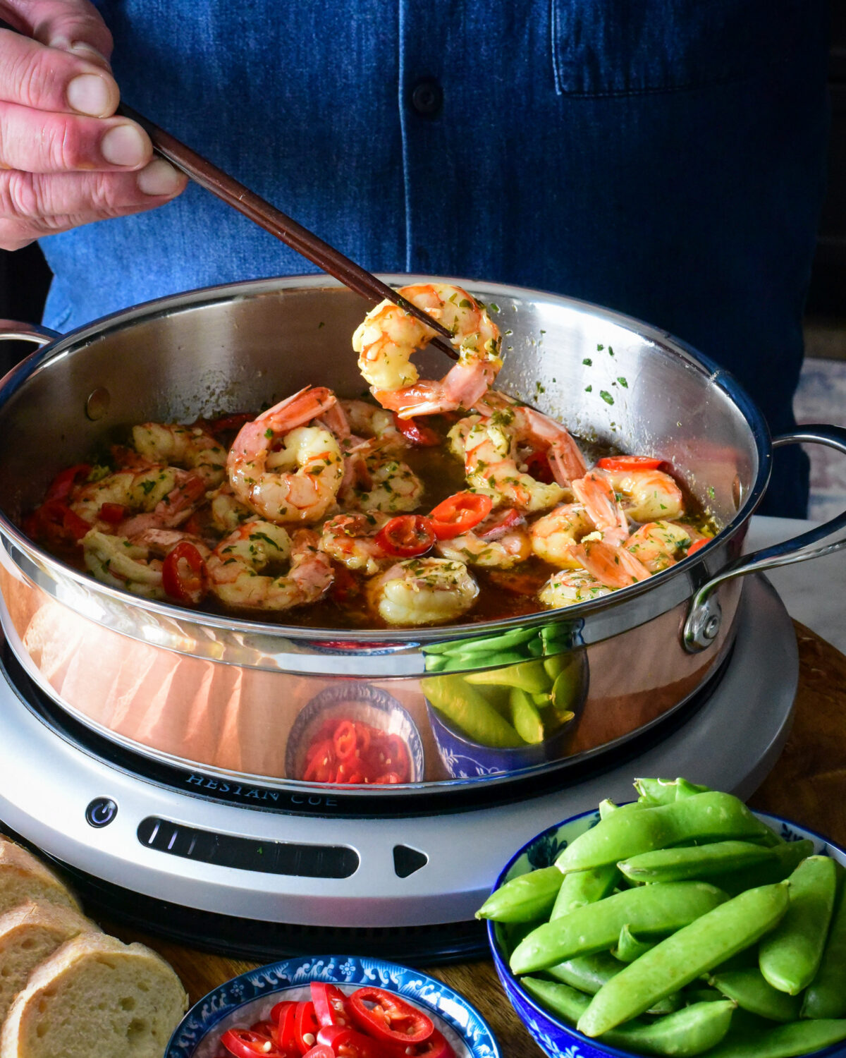 A copper pan with garlic shrimp and one being lifted up.