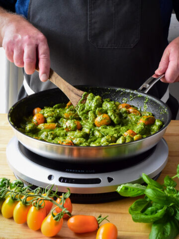 A chef stirring a pan of fried pesto with orange tomatoes on a portable induction burner.