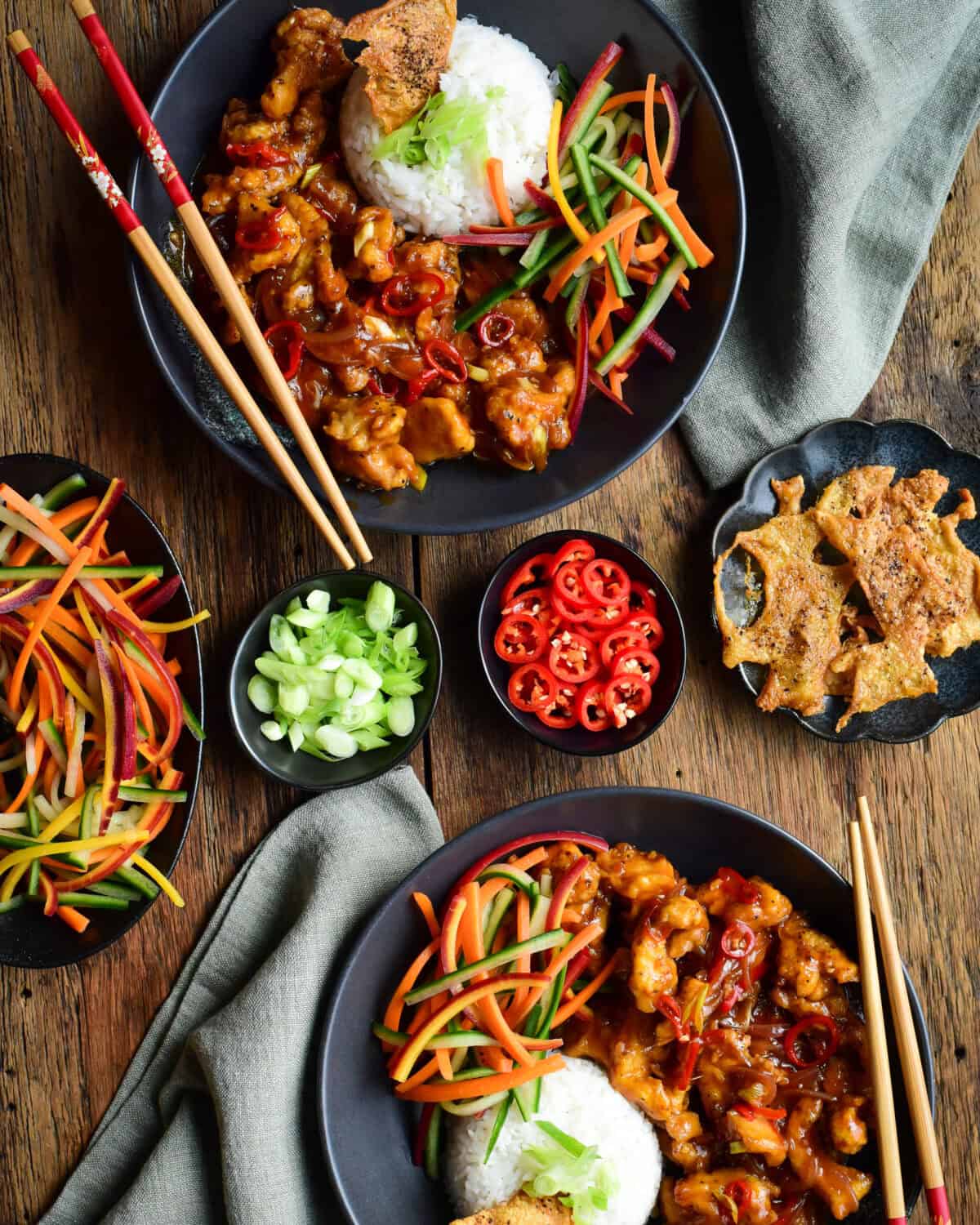 Two bowls of Chili Chicken with Coconut Ginger Rice served with a a carrot and cucumber salad and crispy chicken skins.