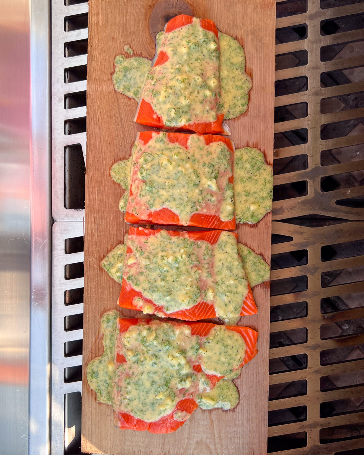 Four salmon portions on a cedar plank with sauce ready to grill.