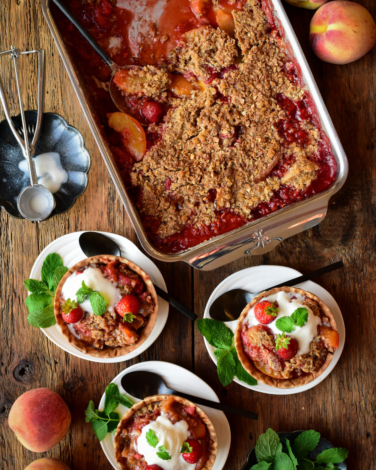 A baking tray with a baked Peach Strawberry Crisp with three bowls served with ice cream and mint.