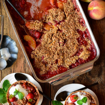 A baking tray with a baked Peach Strawberry Crisp with two bowls served with ice cream and mint.