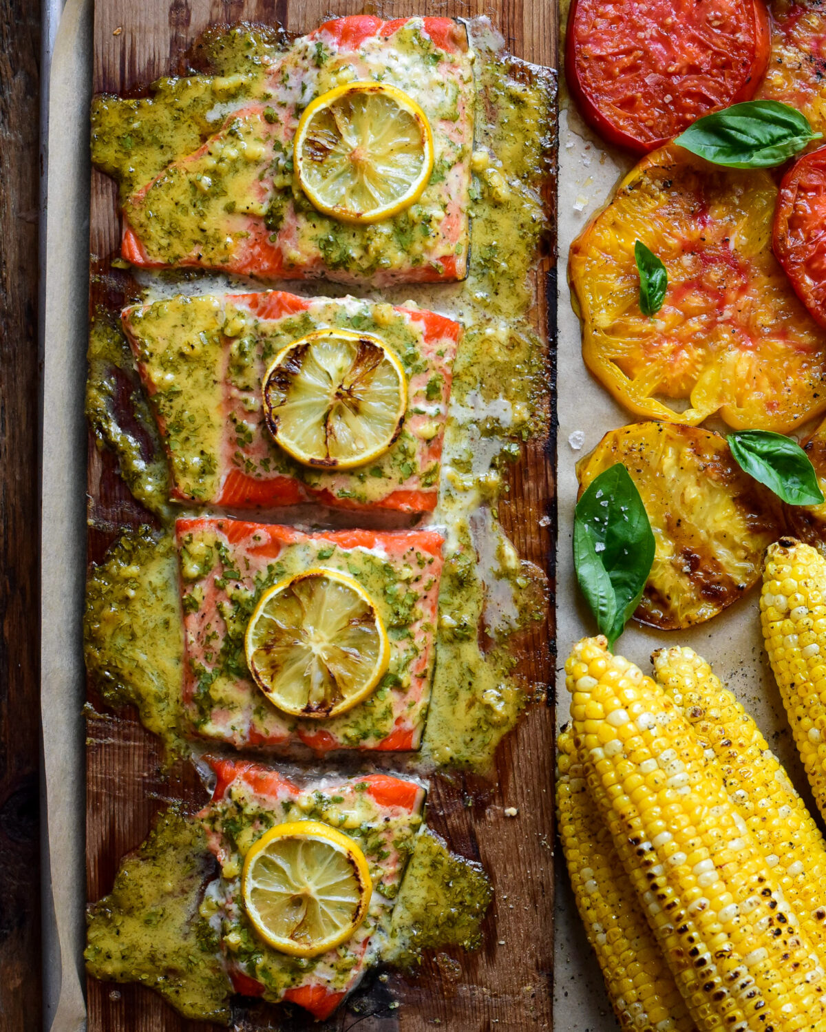 Cedar Plank Sockeye Salmon portioned in four with sauce and lemon slices. Served with grilled corn and tomatoes.