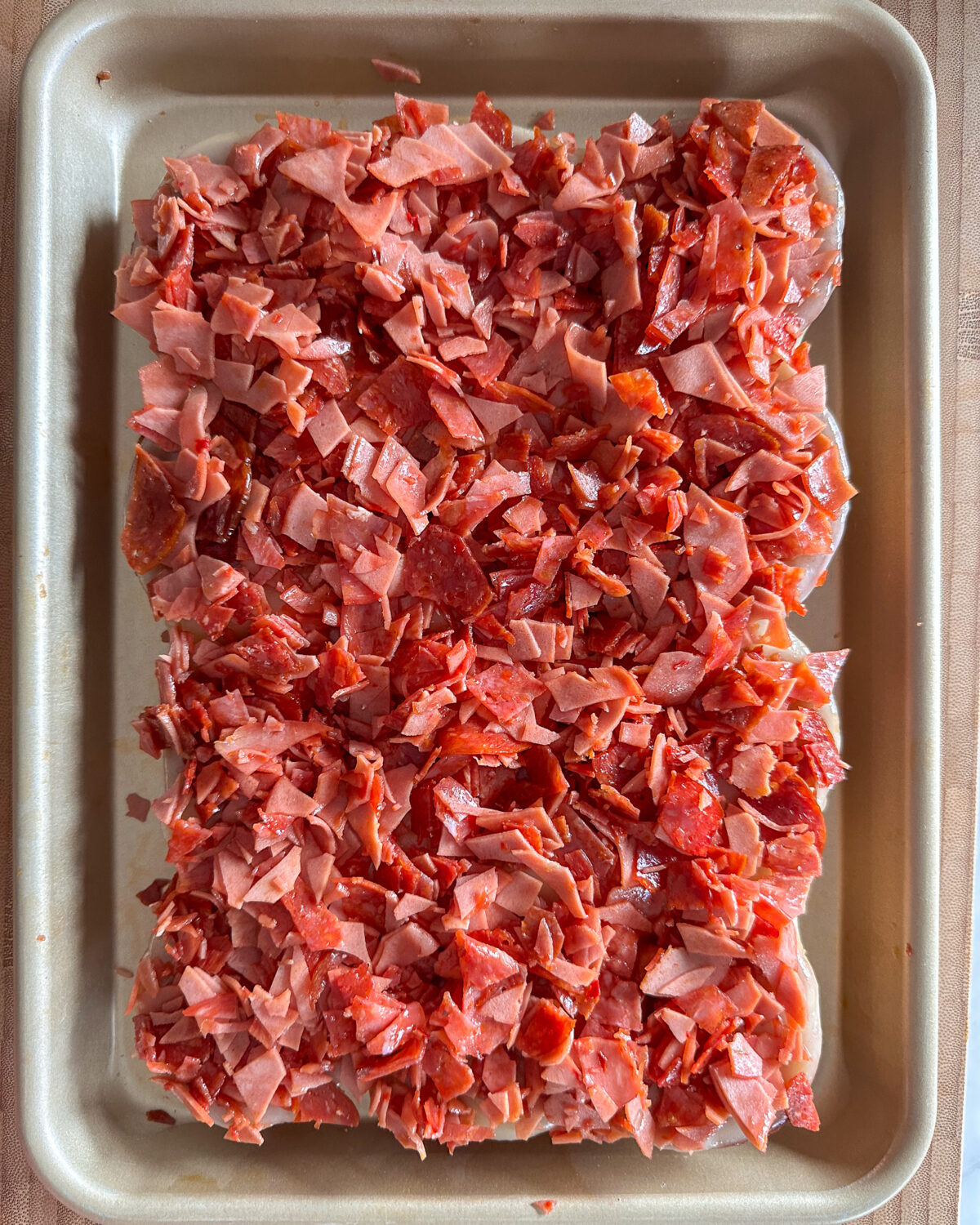 A layer of chopped deli meats spread on toasted slider buns.
