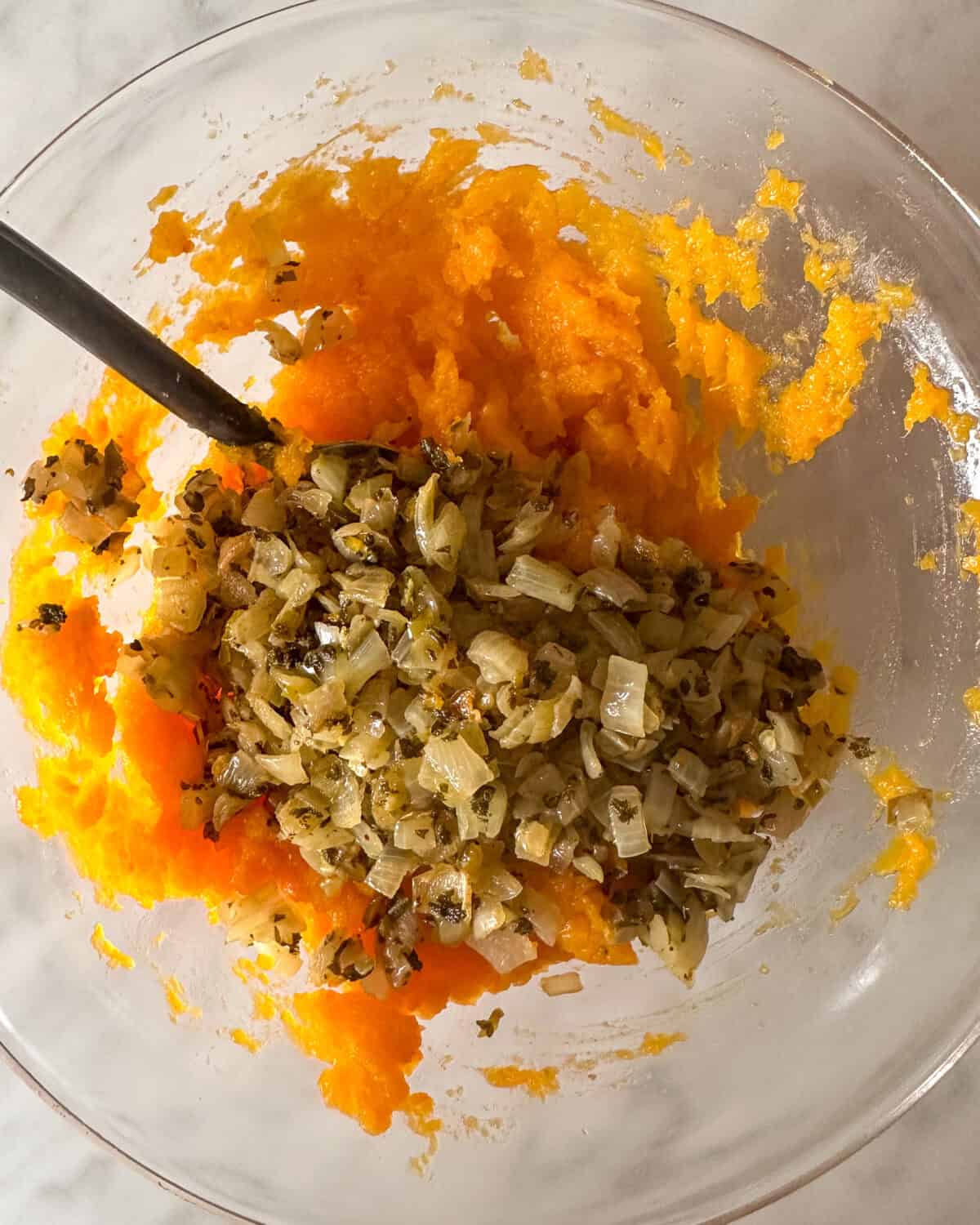 A bowl of mashed squash with an onion sage mixture.