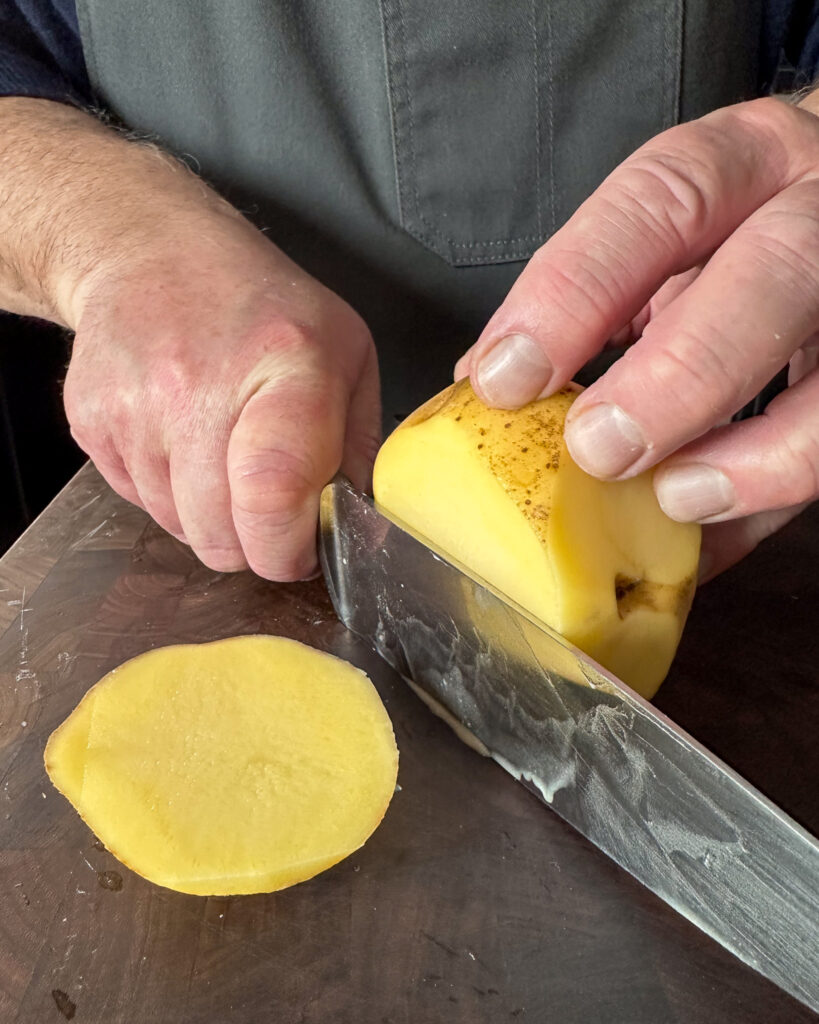 Slice a little off the top and bottom so that the bottom of the potato sits flat on the cutting board and the cutter sits flat on the top.