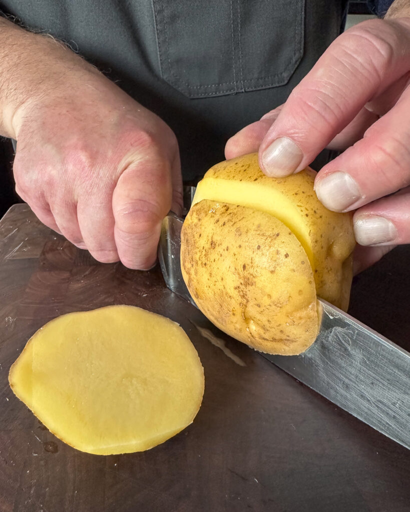 Slice a little off the top and bottom so that the bottom of the potato sits flat on the cutting board and the cutter sits flat on the top.