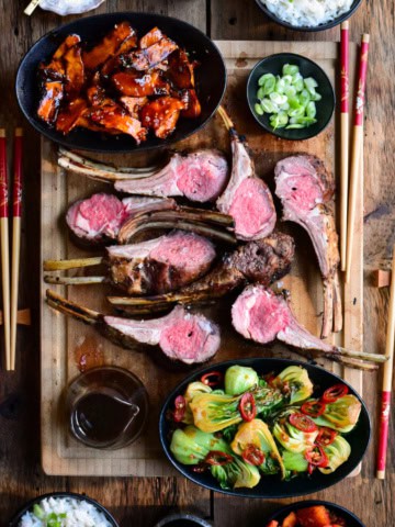 A serving board with two Grilled Frenched Rack of Lamb, cut open and served with Grilled Gochujang Mushrooms and Garlic-Ginger Bok Choy.