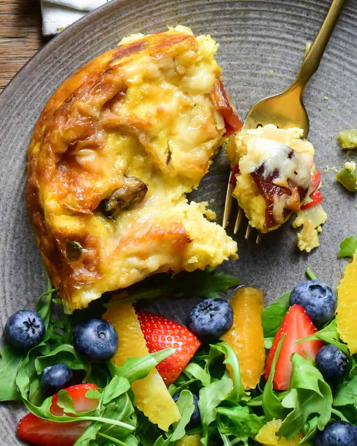 A plated croissant casserole served alongside a fruit and arugula salad.