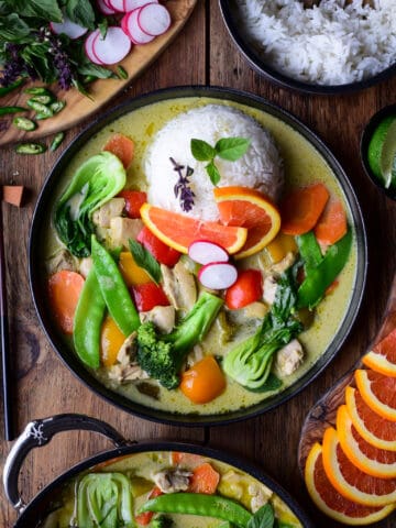 A colourful and vibrant plate of Thai Green Curry Chicken & Vegetables. Served with jasmine rice, Thai basil, orange slices and green chilies.