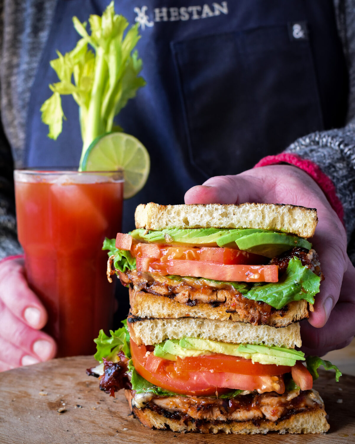 Two haves of a BBQ spicy chicken club sandwiched stacked together with a spicy Caesar cocktail.  