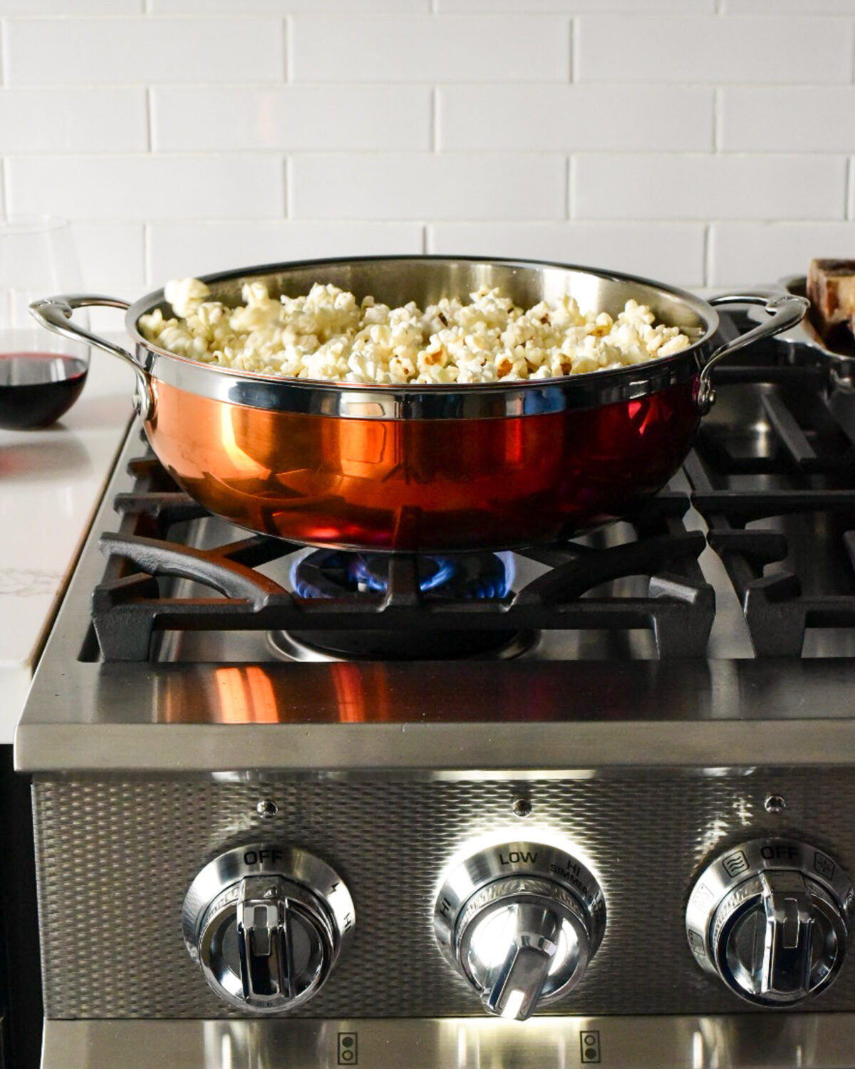 A copper pot with popcorn made on a stove top.