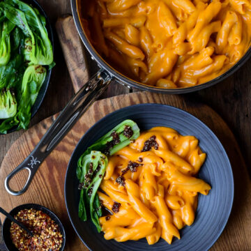 A pot and bowl of creamy Gochujang Mac n Cheese with bok choy and a chili oil drizzle.