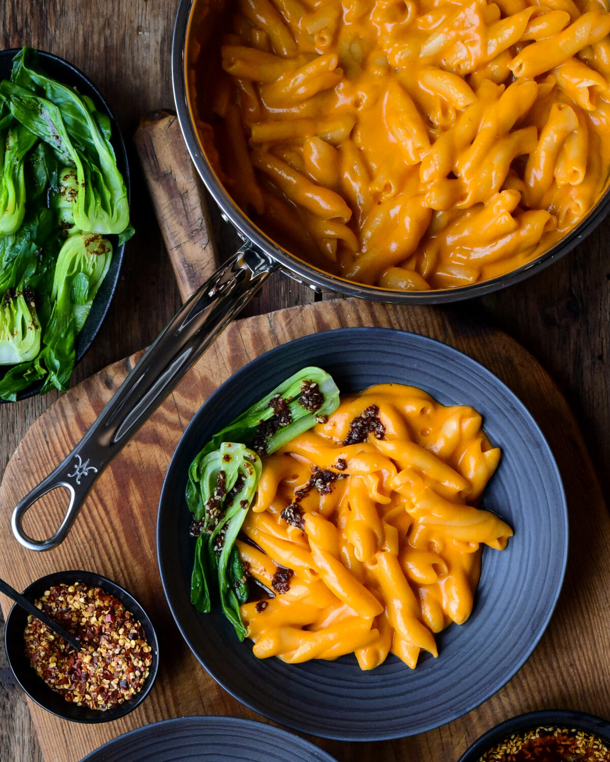 A pot and bowl of creamy Gochujang Mac n Cheese with bok choy and a chili oil drizzle.