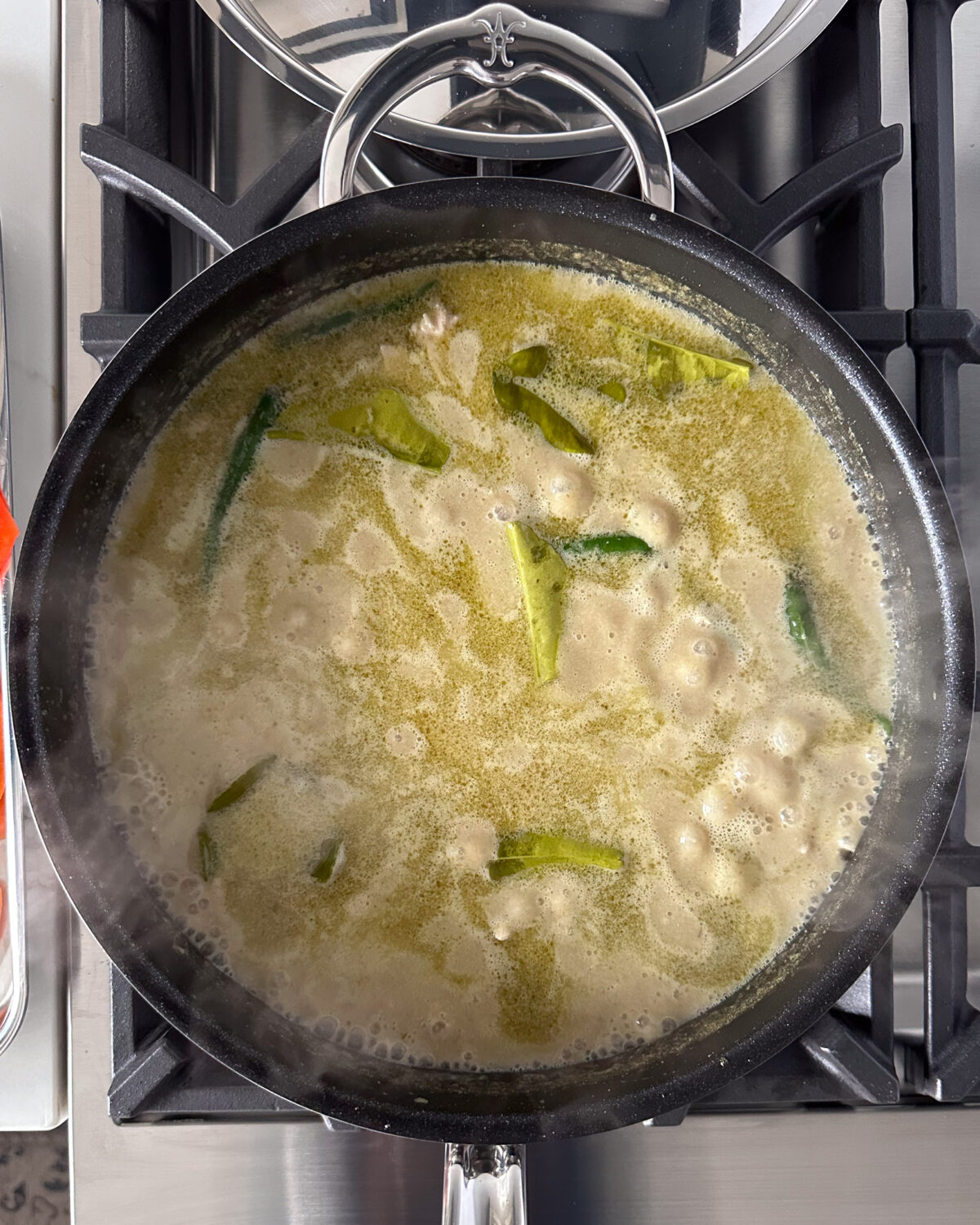 Simmering the curry sauce with green curry paste, garlic, ginger, coconut milk, broth, lime leaves, brown sugar and fish sauce.