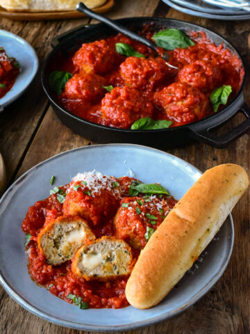 A bowl of Air Fryer Chicken Parmesan Meatballs with a breadstick and a skillet behind with more meatball in sauce.