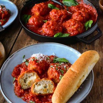 A bowl of Air Fryer Chicken Parmesan Meatballs with a breadstick and a skillet behind with more meatball in sauce.