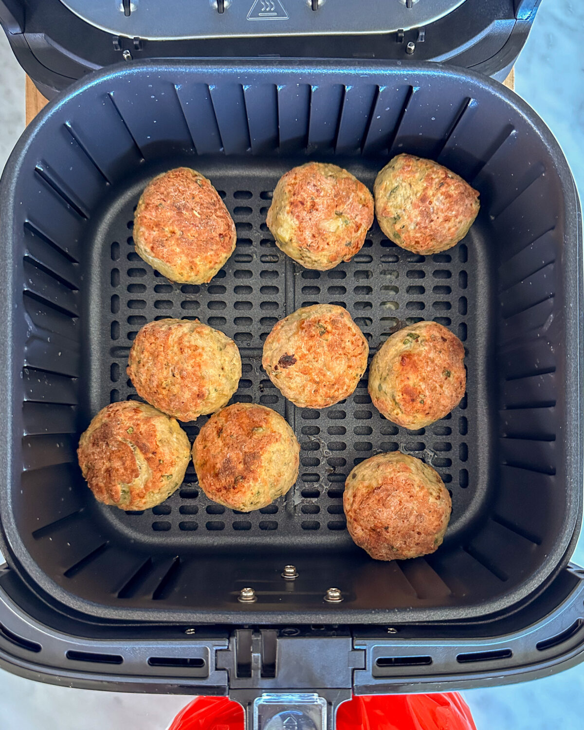 A batch of golden chicken parm meatballs in an air fryer.